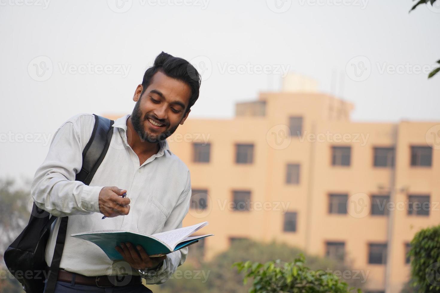 giovane studente di college maschio in piedi fuori al campus e leggendo un libro foto