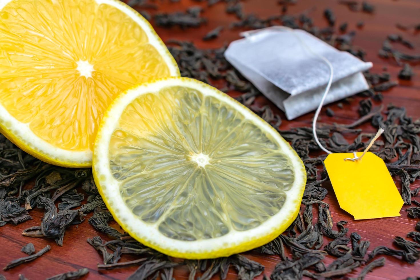 un succoso limone tagliato giace sulle foglie di tè nero con una bustina di tè foto