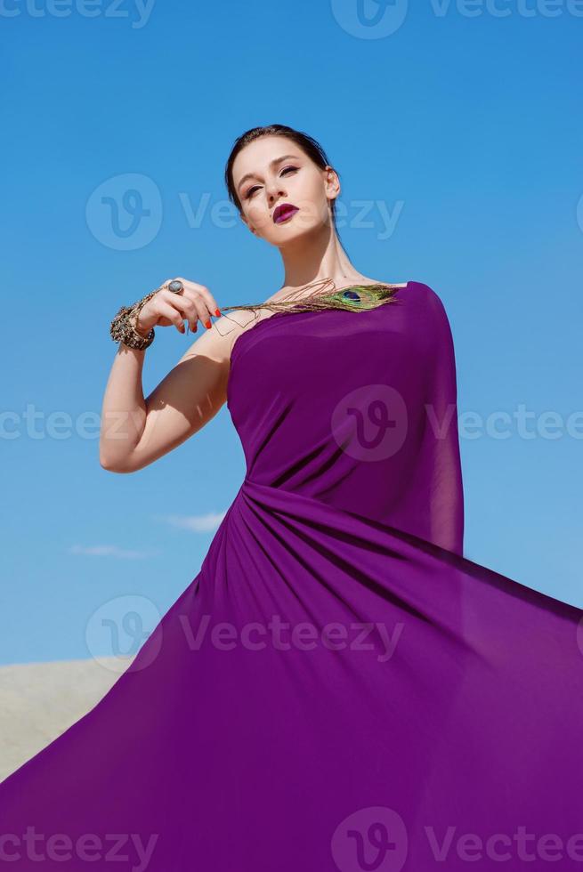 incredibile bella donna bruna con la piuma di pavone in tessuto viola nel deserto. orientale, indiano, moda, concetto di stile foto