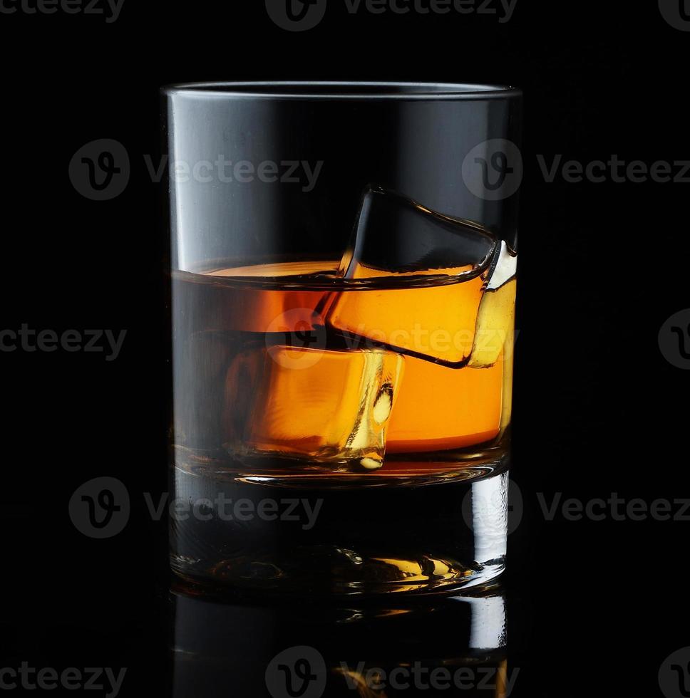 whisky scozzese in un bicchiere elegante con cubetti di ghiaccio su sfondo nero. foto