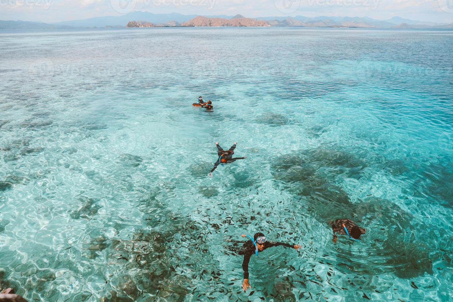 turisti asiatici che nuotano e fanno snorkeling sull'acqua di mare trasparente foto