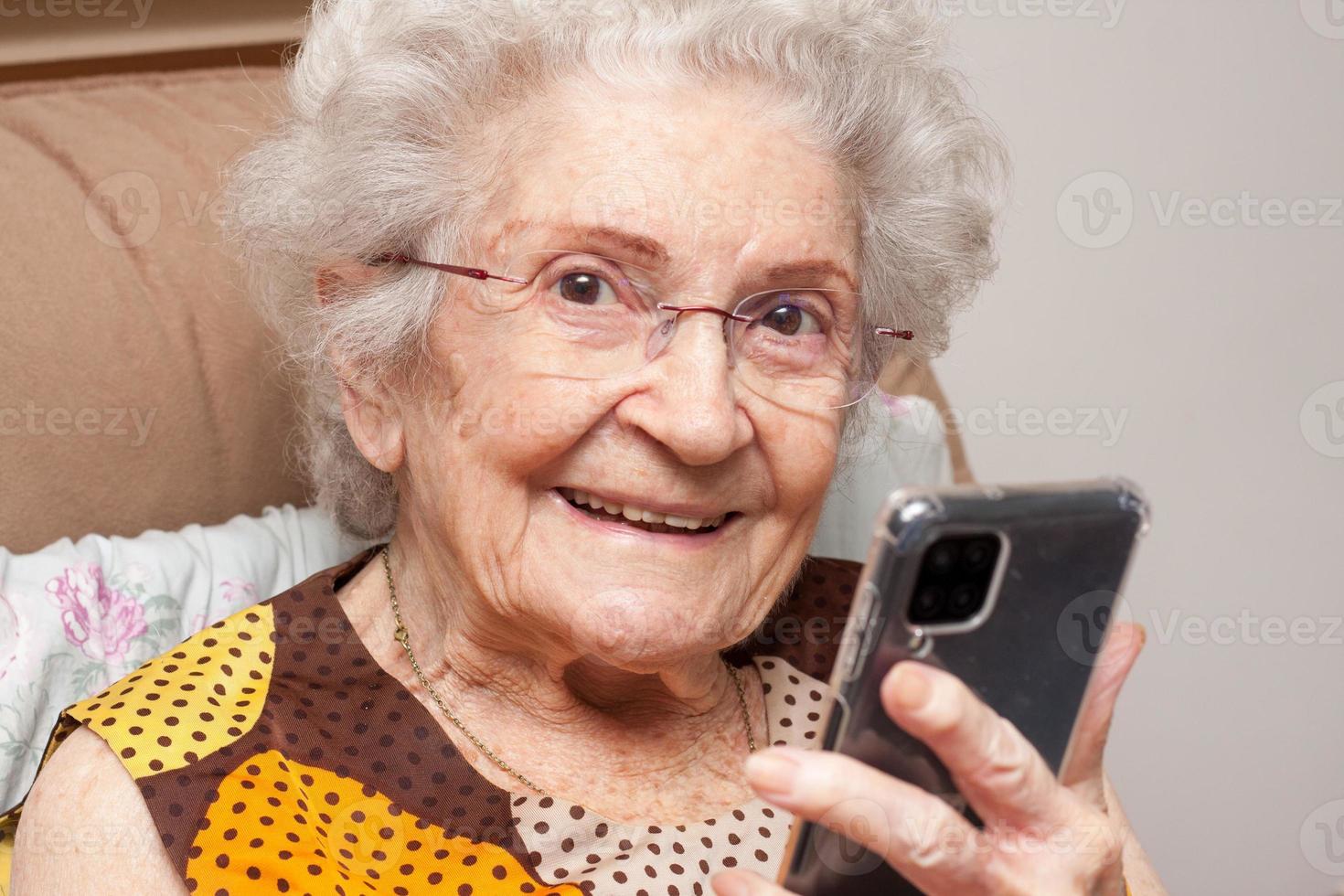 signora anziana a casa seduta su una sedia guardando il suo smartphone foto