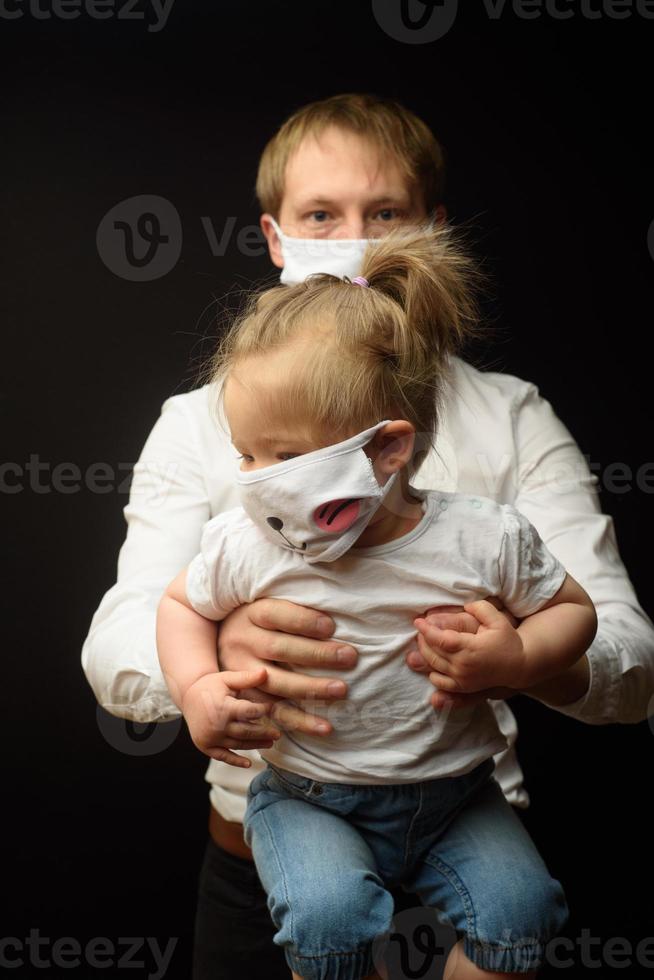 il padre con una maschera medica tiene la sua piccola figlia. il concetto di protezione dei bambini durante l'epidemia di coronavirus foto