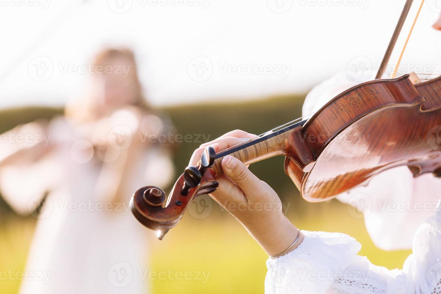 la bambina suona il violino all'aperto con il giardino sullo sfondo in una soleggiata giornata estiva. immagine con messa a fuoco selettiva e spazio di copia. foto