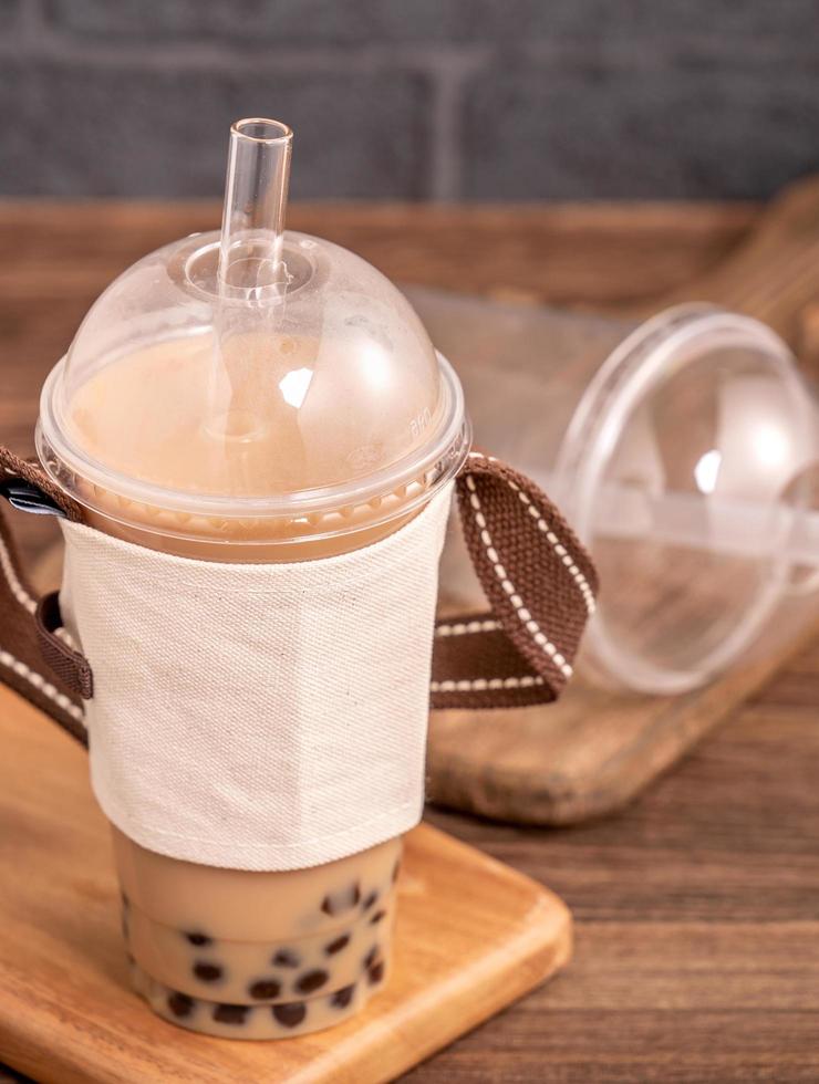 da asporto con il concetto di articolo usa e getta popolare bevanda taiwan tè al latte con bolle con bicchiere di plastica e paglia su sfondo tavolo in legno, primo piano, spazio di copia foto