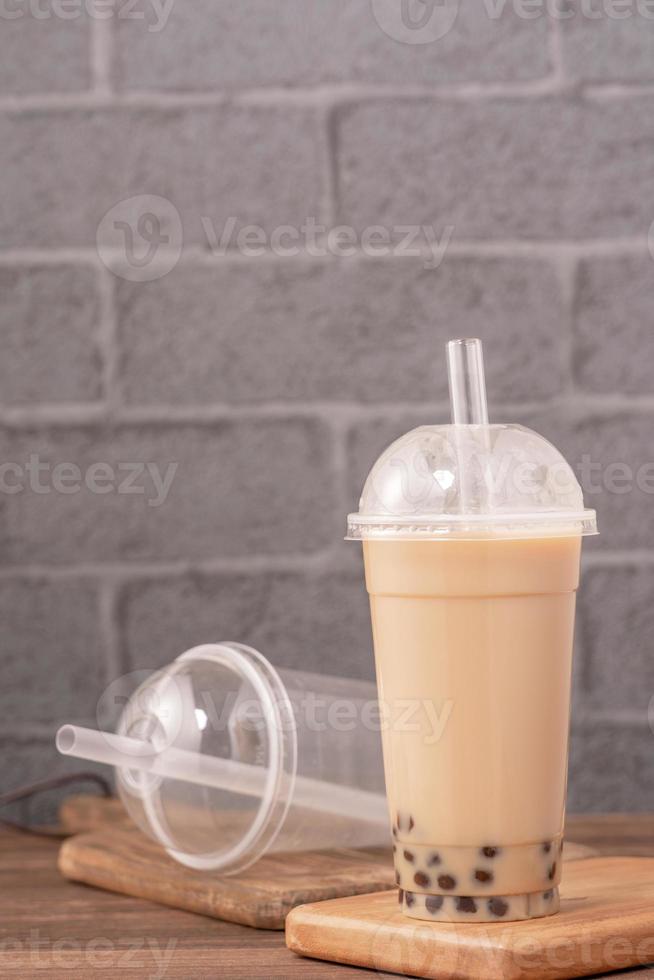 da asporto con il concetto di articolo usa e getta popolare bevanda taiwan tè al latte con bolle con bicchiere di plastica e paglia su sfondo tavolo in legno, primo piano, spazio di copia foto