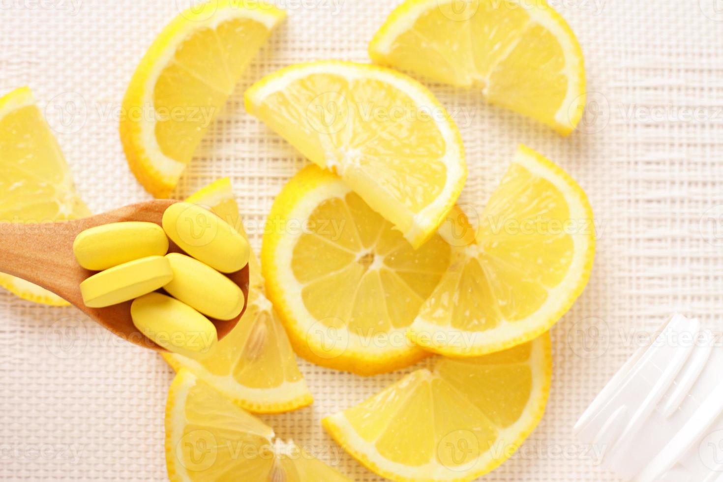 vitamine gialle su cucchiaio e fette di limone come sfondo foto