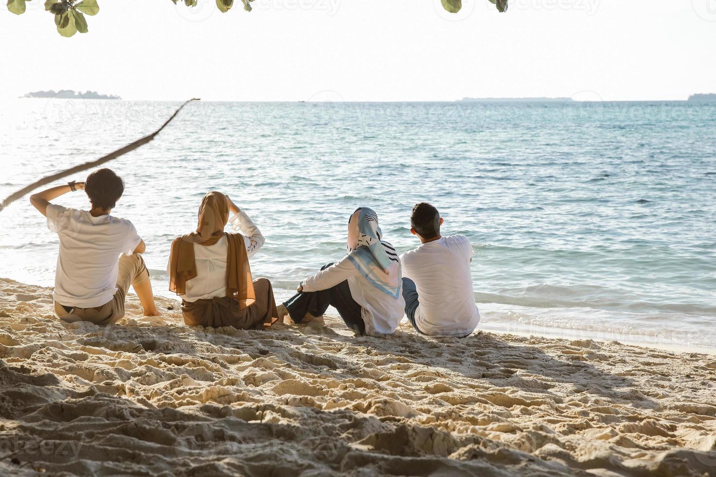 gruppo di persone sedute e rilassanti sulla spiaggia di sabbia bianca mentre si godono le vacanze estive in spiaggia foto