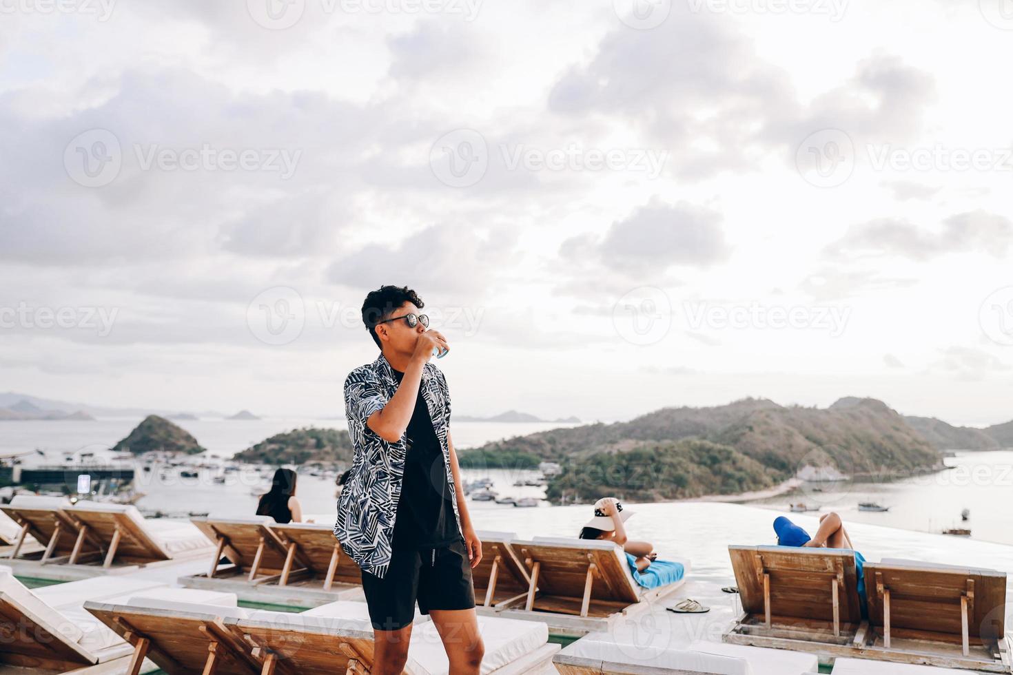 uomo asiatico che beve durante le vacanze estive con sfondo sfocato delle isole e molte barche sul mare foto