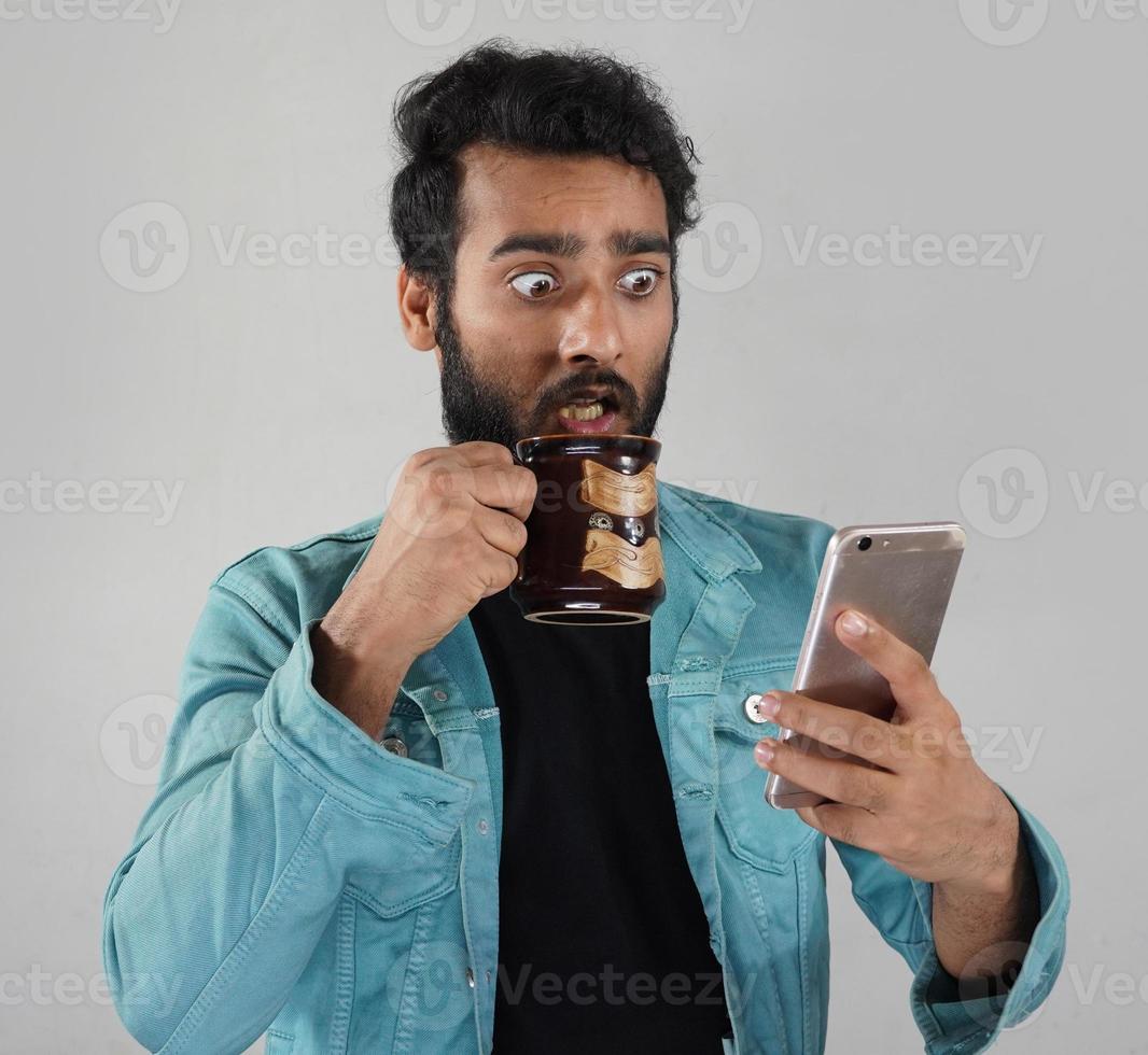 un uomo con una tazza di caffè e un cellulare che guarda le notizie ed è scioccato a causa delle cattive notizie foto