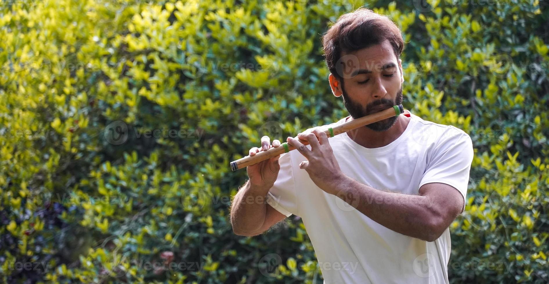 musicista indiano maschio che suona il bansuri con una maglietta bianca. tiro all'aperto su sfondo verde foto