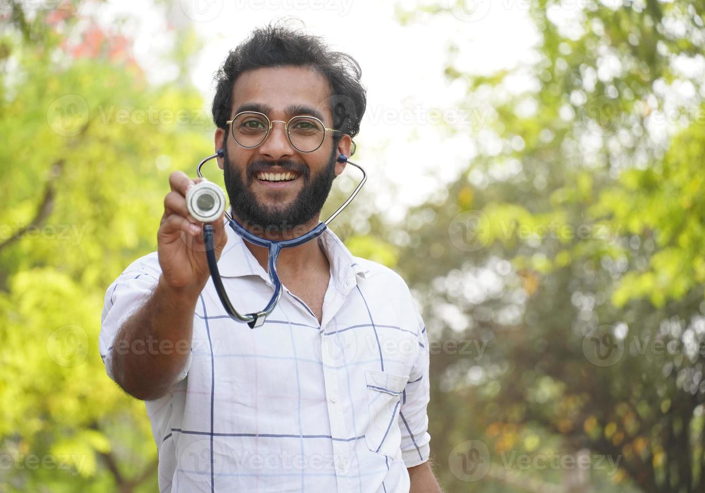 uno studente uscito che mostra lo stetoscopio-studente universitario con lo stetoscopio e che mostra il concetto di educazione medica del segno di successo foto