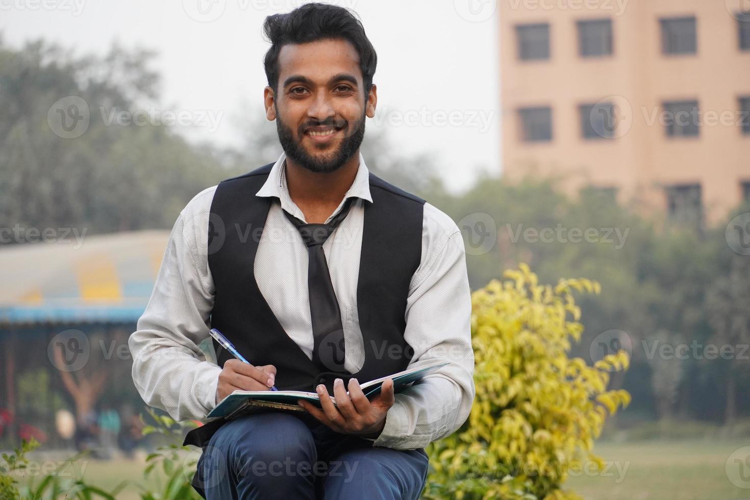 bel ragazzo della scuola o del college seduto sulla panchina con libro e borchie in un parco foto