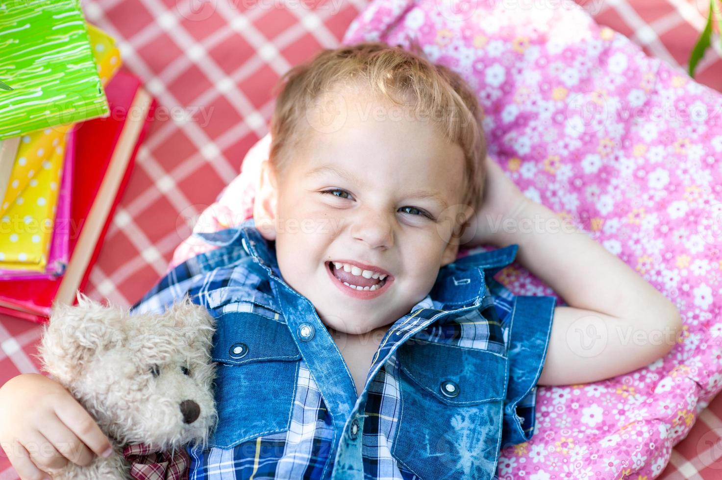 un ragazzino carino giace su un plaid, abbraccia il suo orsacchiotto e guarda il cielo. il concetto di vacanze in famiglia nella natura. foto