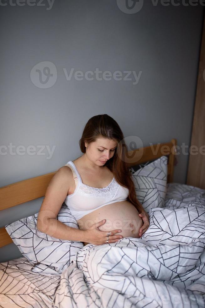 una ragazza incinta si aggrappa alla sua pancia e si preoccupa prima di partorire durante un krantin. autoisolamento in casa. foto