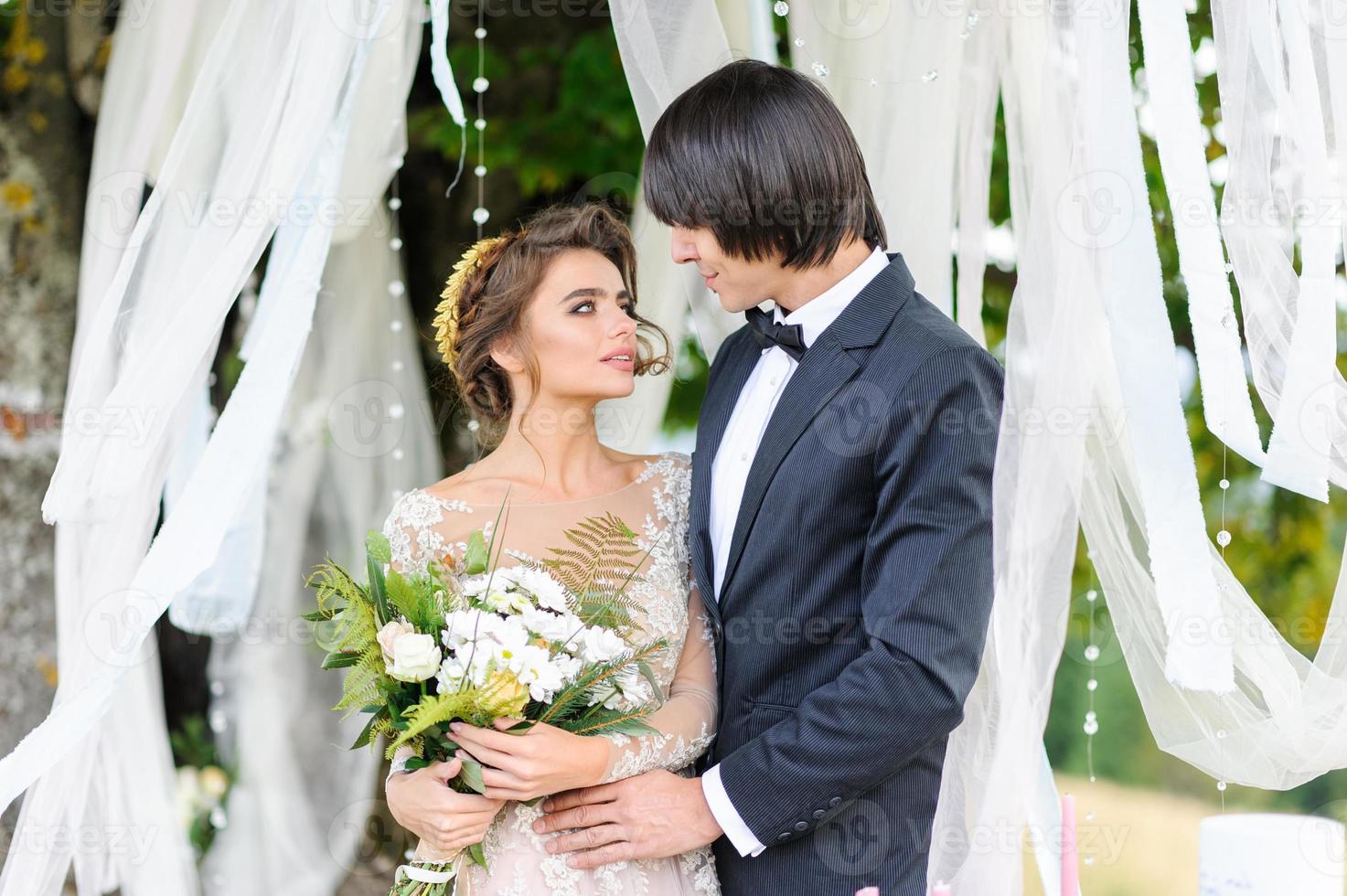 gli sposi si abbracciano sotto una vecchia quercia. servizio fotografico di matrimonio in montagna. accanto a loro viene preparato l'arredamento per la cerimonia. foto