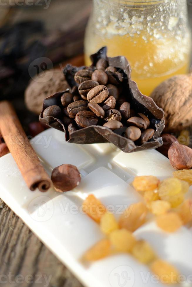 cucchiaio di legno con miele su un tavolo di legno accanto a piastrelle di cioccolato bianco, uvetta, bastoncini di cannella foto