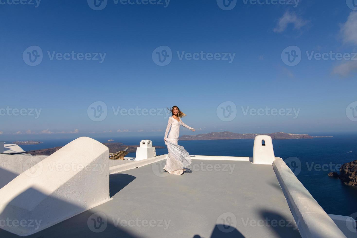 bella sposa in abito bianco in posa sul tetto della casa sullo sfondo del mar mediterraneo a thira, santorini. foto