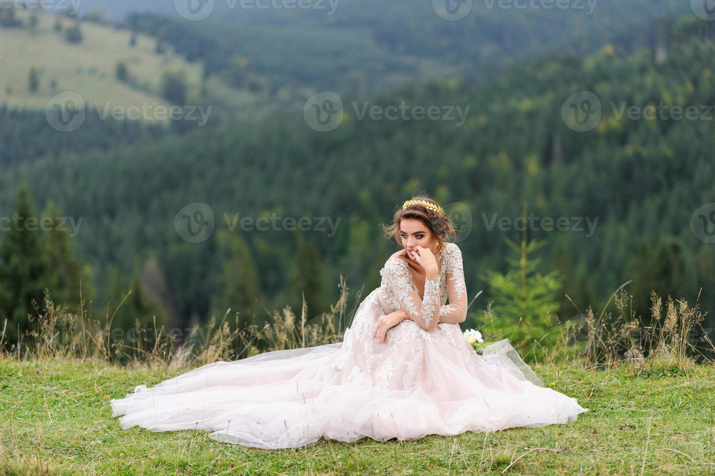 bella sposa in un vestito rosa si siede su uno sfondo di montagne. foto