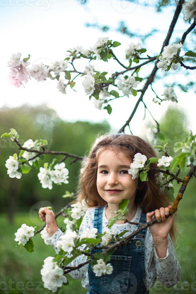 una graziosa bambina di 5 anni in un frutteto di mele bianco in fiore in primavera. primavera, frutteto, fioritura, allergia, profumo di primavera, tenerezza, cura della natura. ritratto foto