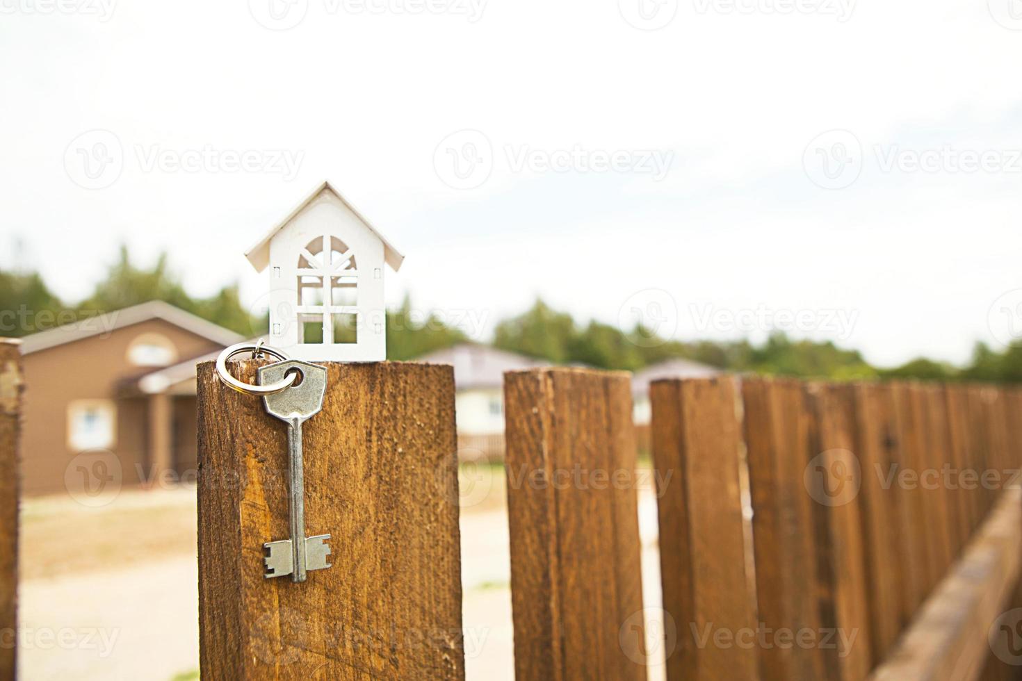 piccola figura di casa in legno bianco sul recinto con chiave per alloggi sullo sfondo dei cottage. costruzione, progettazione, progetto, trasloco in nuova casa, mutuo, affitto e acquisto di immobili. copia spazio foto