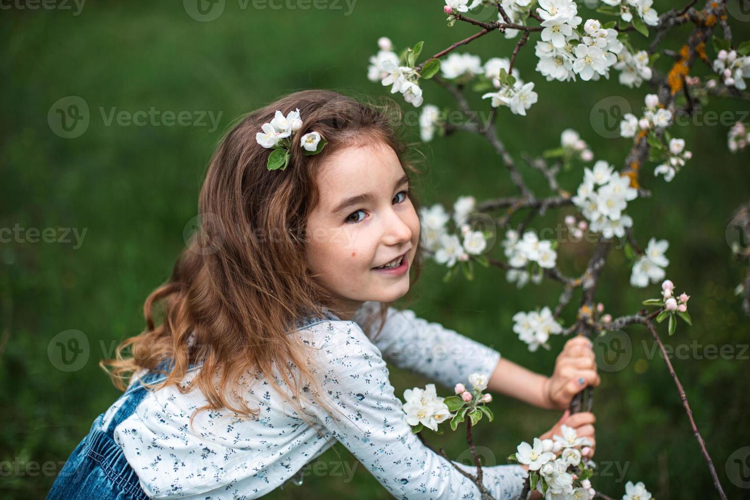 una graziosa bambina di 5 anni in un frutteto di mele bianco in fiore in primavera. primavera, frutteto, fioritura, allergia, profumo di primavera, tenerezza, cura della natura. ritratto foto