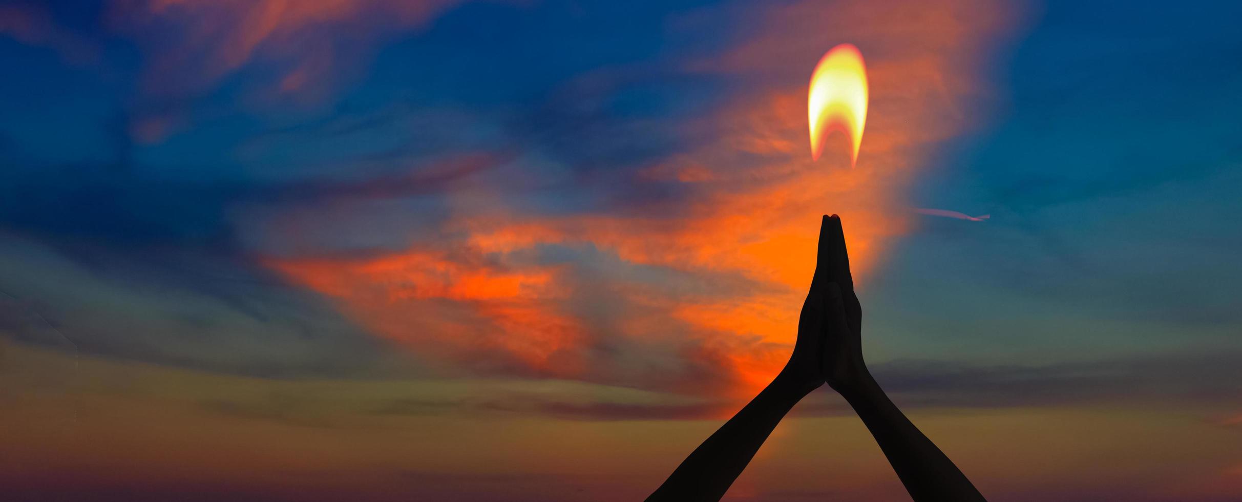 silhouette di mani che pregano su sfondo tramonto e concetto di fiamma di candela. luce di speranza. foto