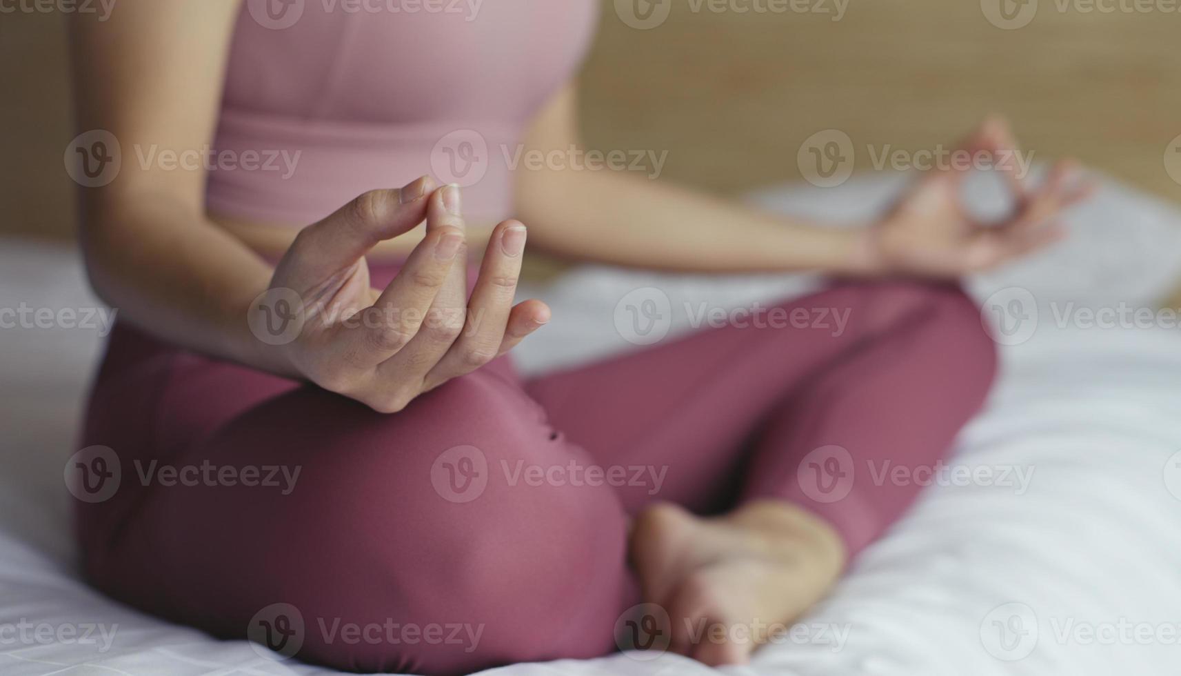 mano ravvicinata della giovane donna seduta nella posa del loto sul letto di casa. allenamento mattutino in camera da letto. foto