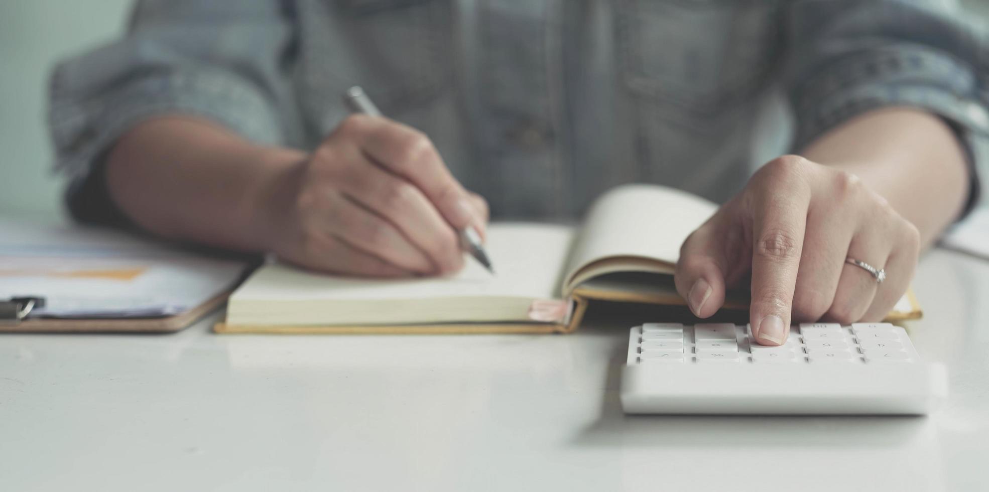 primo piano donna asiatica che lavora con la mano di dati finanziari utilizzando la calcolatrice e scrivendo prendi nota con calcolare. concetto finanziario e contabile aziendale. foto