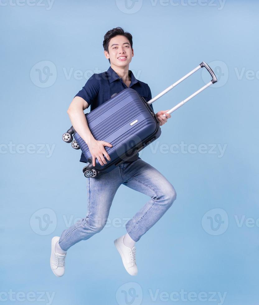 immagine di giovane uomo asiatico che tiene la valigia su sfondo blu, concetto di viaggio foto