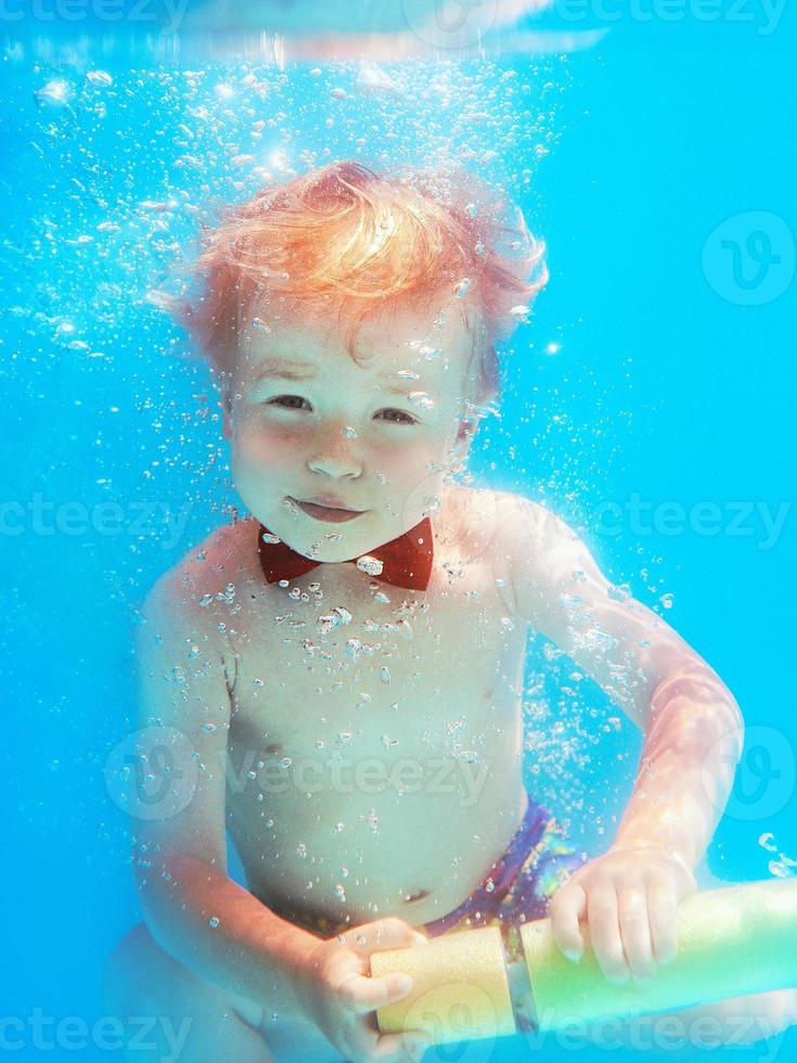 bambino piccolo con farfalla rossa che si tuffa sott'acqua in piscina, impara a nuotare. concetto di sport e vacanza foto