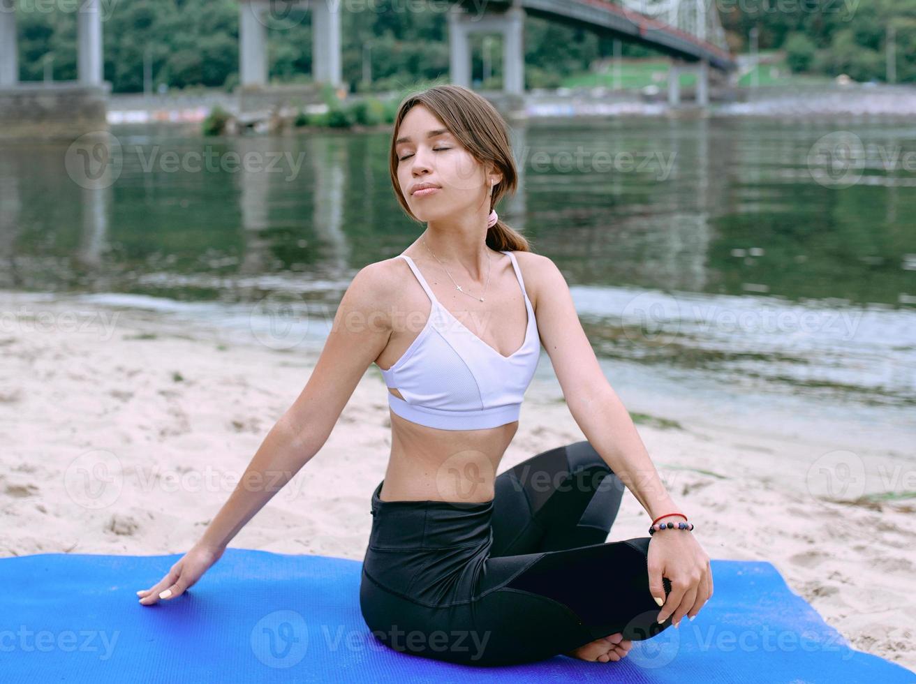giovane donna in forma in abbigliamento sportivo in diverse asana yoga all'aperto sulla spiaggia vicino al fiume. concetto di yoga e sport foto