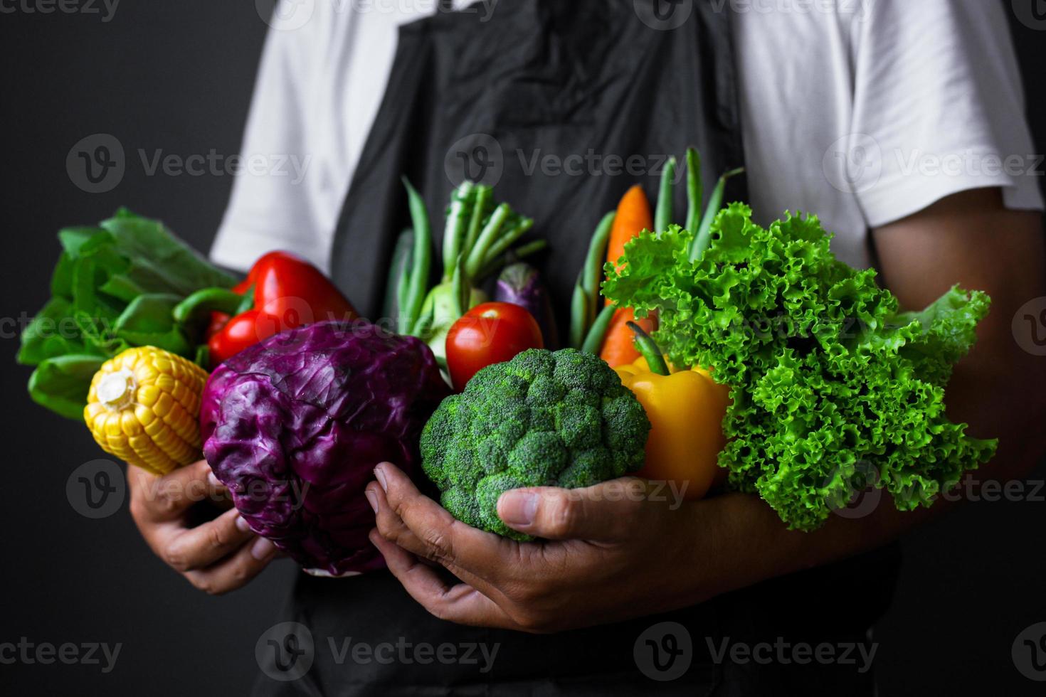 uomo che indossa un grembiule che tiene varie verdure in entrambe le mani foto