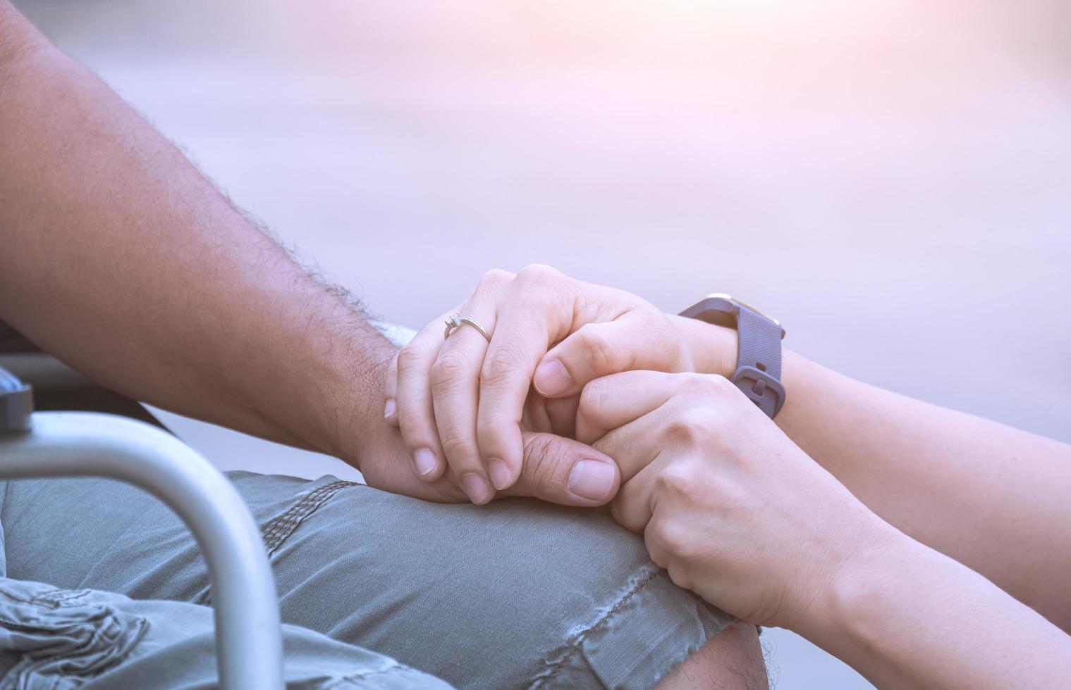 immagine ravvicinata delle mani della donna che tengono la mano del marito sulla sedia a rotelle durante la riabilitazione per incoraggiamento nell'area esterna foto