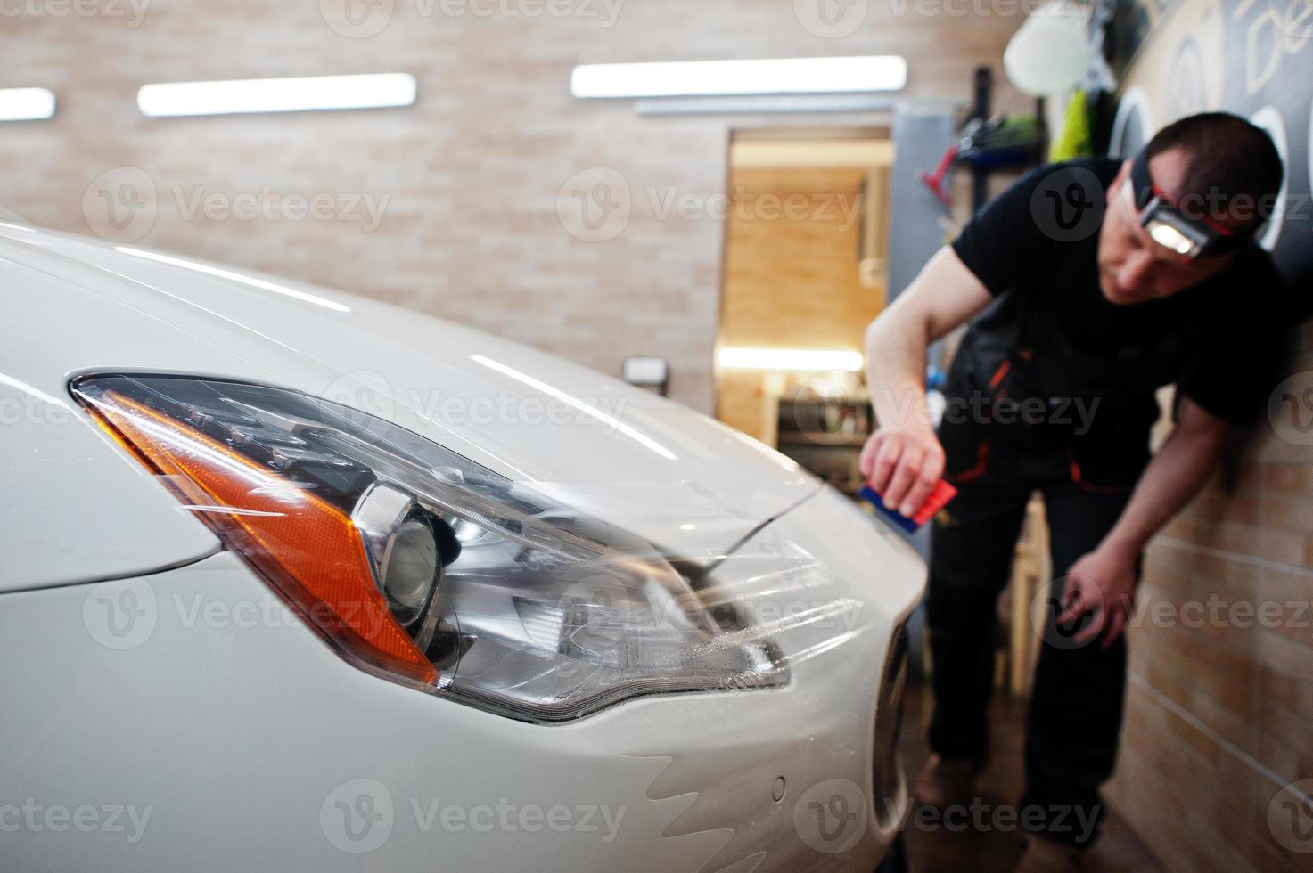 l'operaio nei dettagli il garage ha messo la copertura in pellicola anti-ghiaia in poliuretano in un'auto di lusso bianca. foto