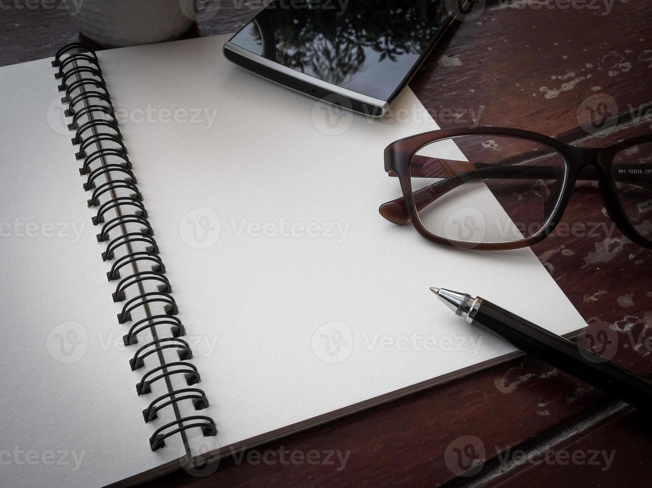 area di lavoro con occhiali, penna, smartphone e tazza di caffè, carta per appunti e taccuino sul vecchio tavolo di legno foto