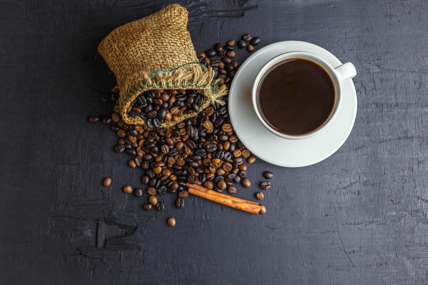 chicchi di caffè in sacchetto di sacco marrone con tazza di caffè su sfondo nero. foto