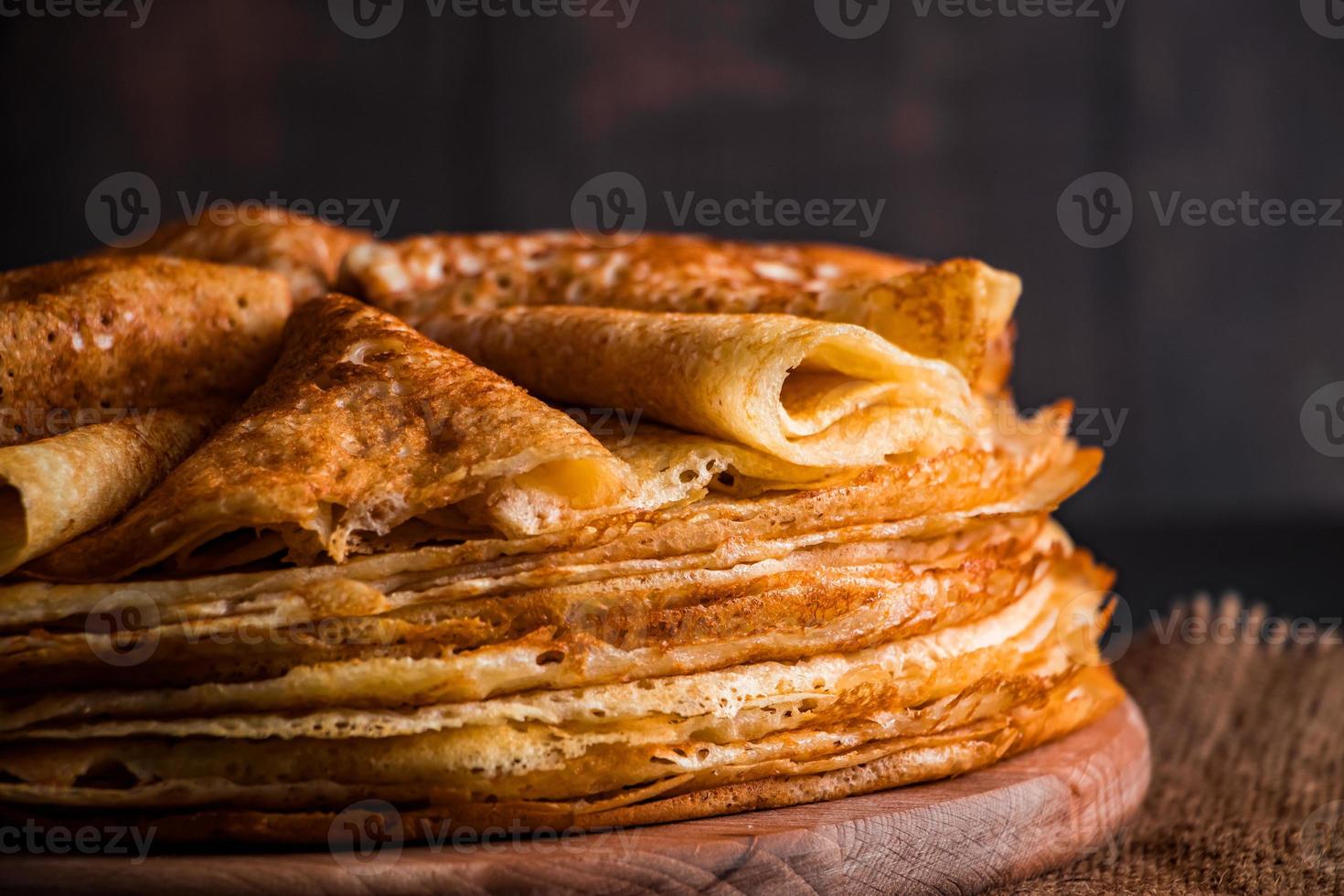 una pila di frittelle sottili su uno sfondo di legno scuro. un piatto tradizionale di crepes per la festa maslenitsa. foto