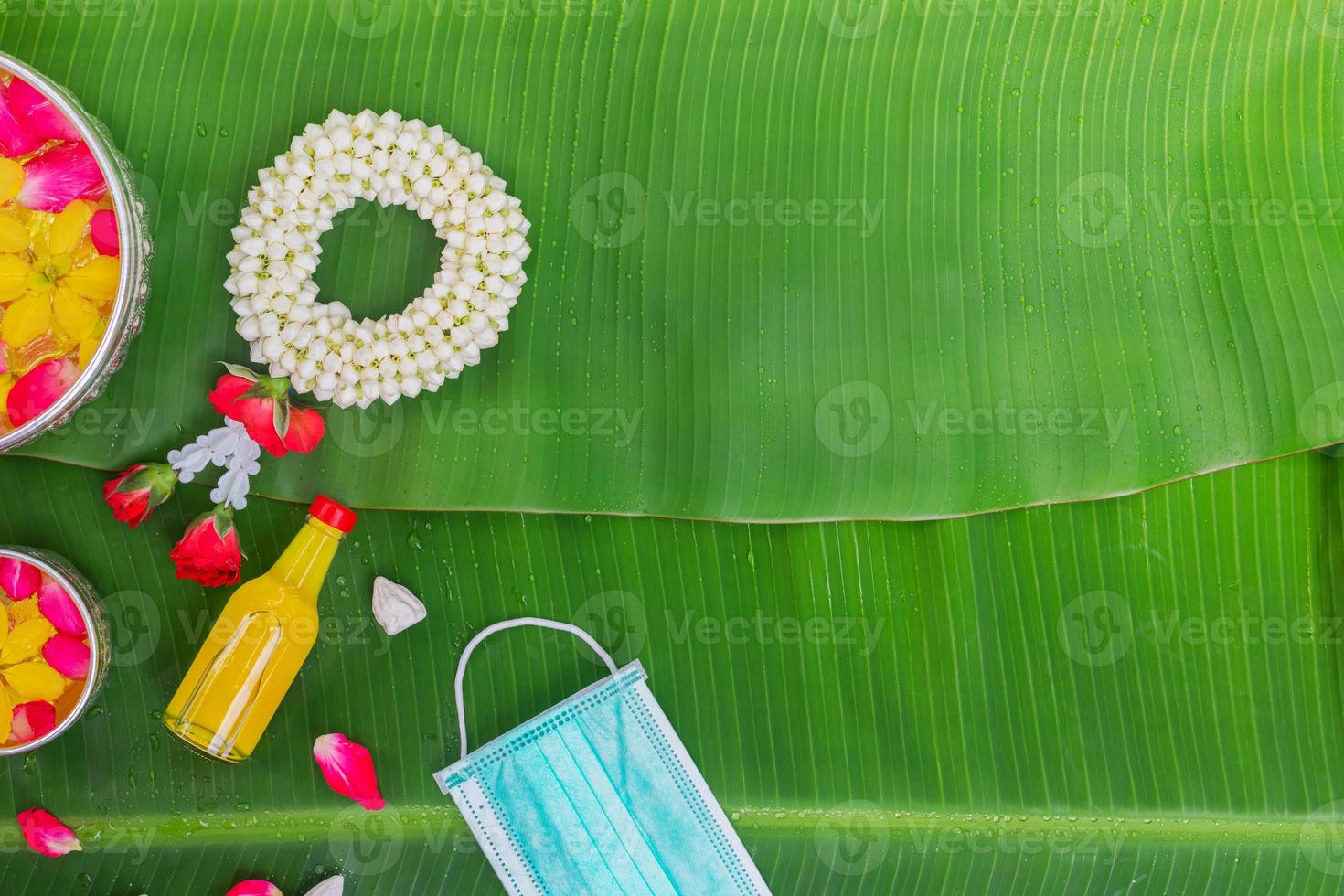 sfondo del festival songkran con fiori di ghirlanda di gelsomino in una ciotola di acqua, profumo e calcare su uno sfondo verde foglia di banana bagnata. foto