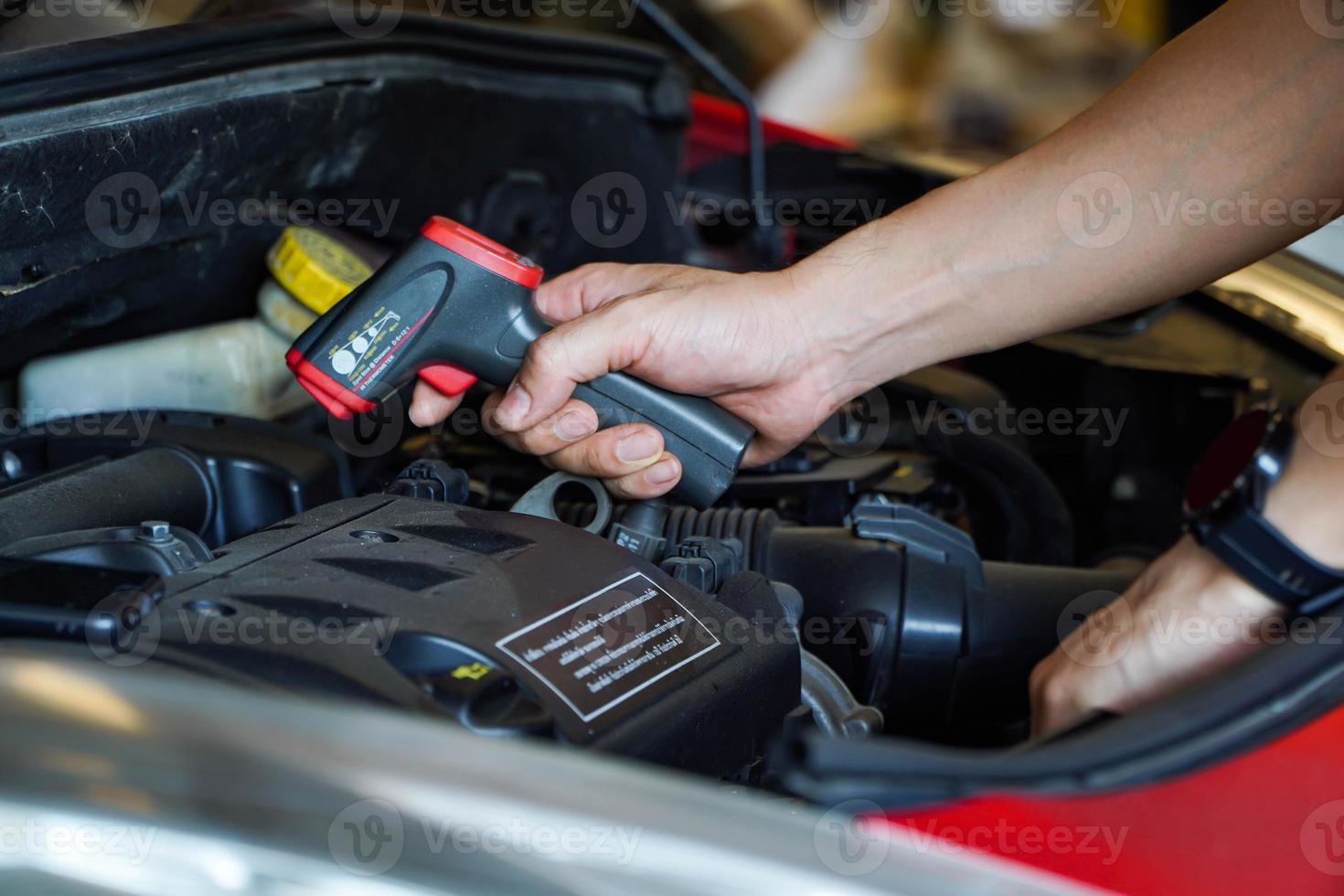 la mano del tecnico tiene un termometro digitale, che misura il calore del motore. Misurazione della temperatura del motore nel servizio dell'auto foto