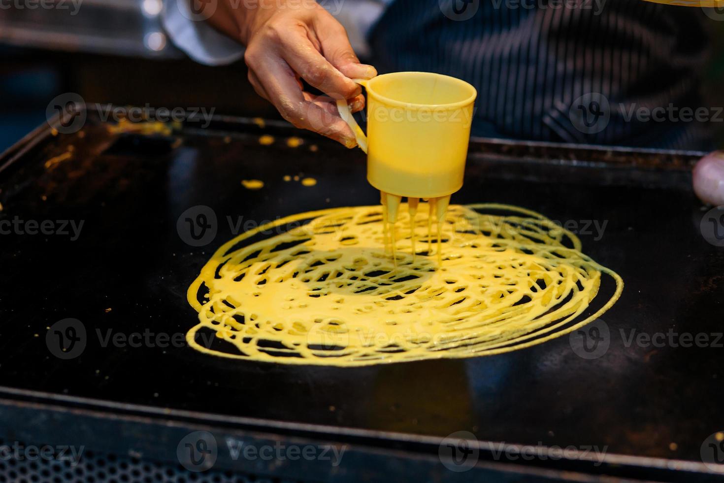 un cuoco fa un movimento circolare per creare frittelle di pizzo o roti jala come è comunemente noto in Malesia foto