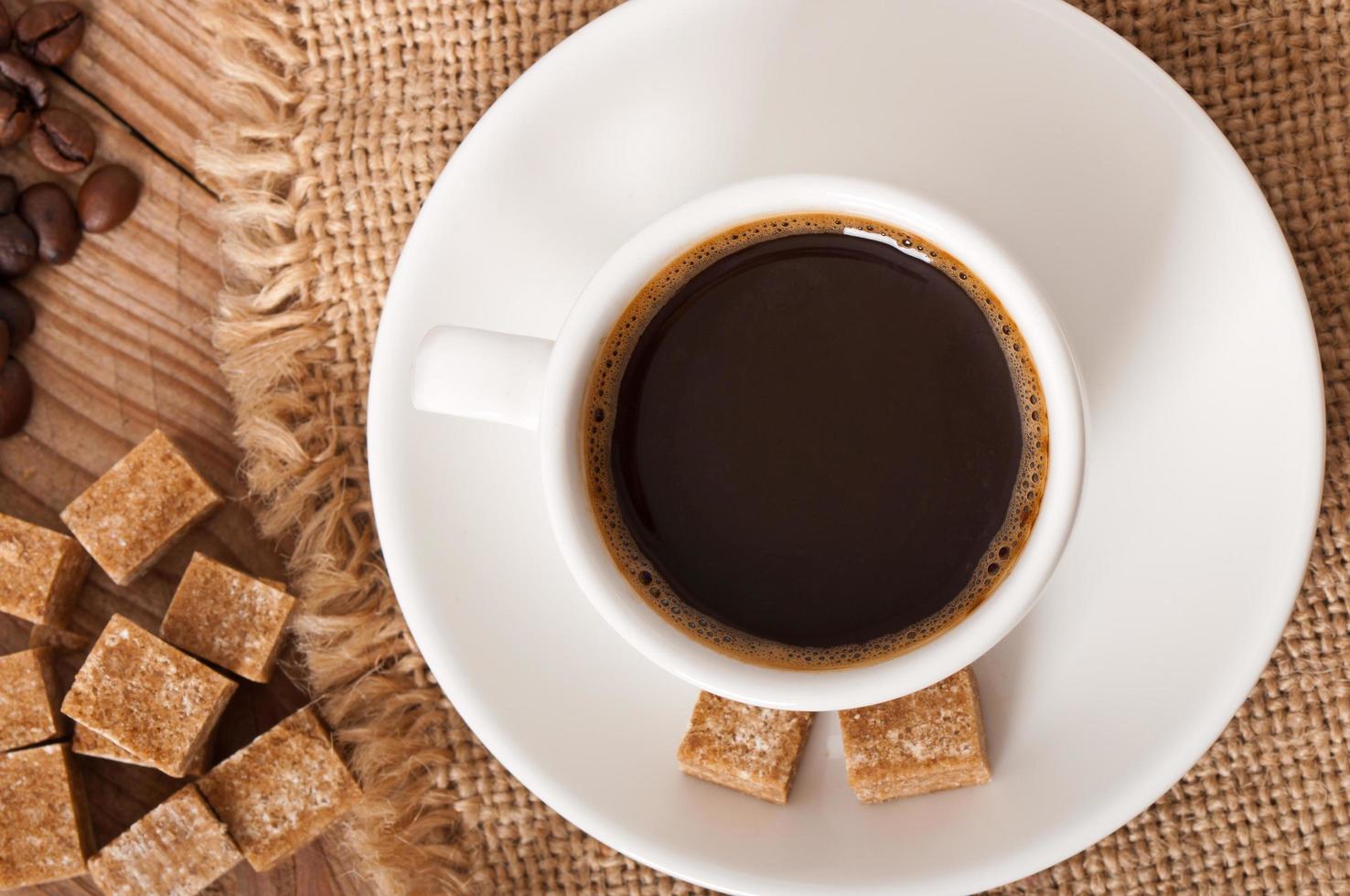 vista del primo piano di una tazza di caffè, zucchero di canna e chicchi di caffè foto