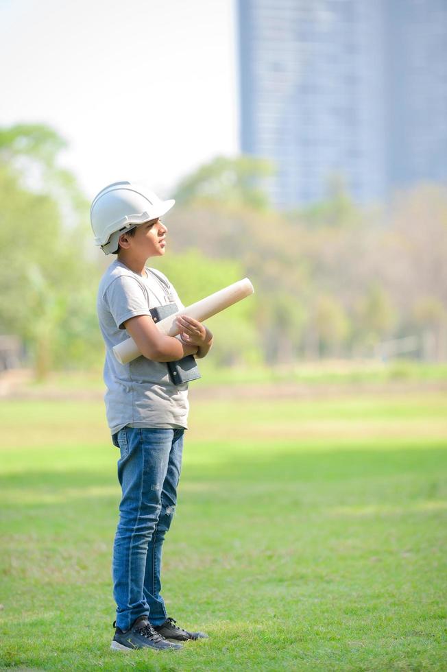 un ragazzo mezzo indiano che indossa un casco tiene un progetto e si aspetta che in futuro sarà un ingegnere per costruire edifici foto