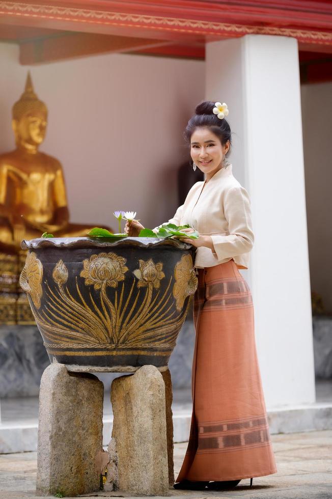 La donna tailandese in vestito tailandese sta tenendo il fiore di loto nel tempio durante la preghiera e si diverte nell'acqua per celebrare il festival dell'acqua di Songkran foto