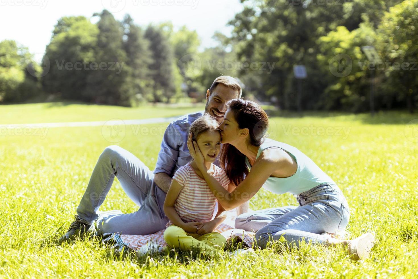 giovane famiglia felice con la piccola figlia carina che si diverte nel parco in una giornata di sole foto