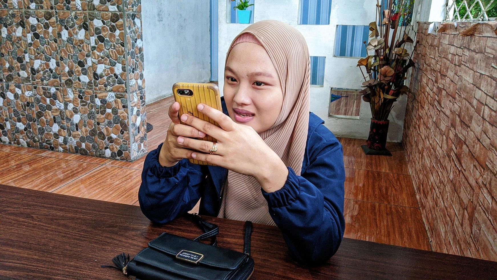 cianjur regency, west java, indonesia il 7 aprile 2022 - una donna musulmana indonesiana che indossa un hijab tiene in mano uno smartphone. foto