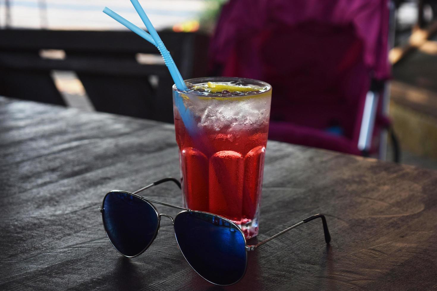 cocktail rinfrescante con una cannuccia, cubetti di ghiaccio e una fetta di limone e occhiali da sole foto