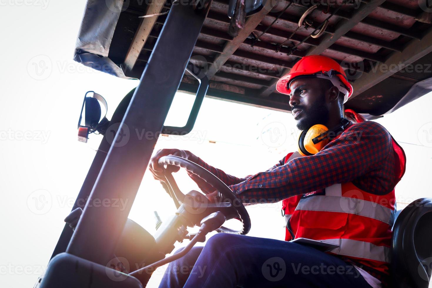 uomo lavoratore industriale che indossa giubbotto rosso neon luminoso di sicurezza e casco che guida un'auto per carrelli elevatori presso l'industria della fabbrica di piante, maschio ingegnere afroamericano che lavora presso il cantiere di container di carico logistico. foto