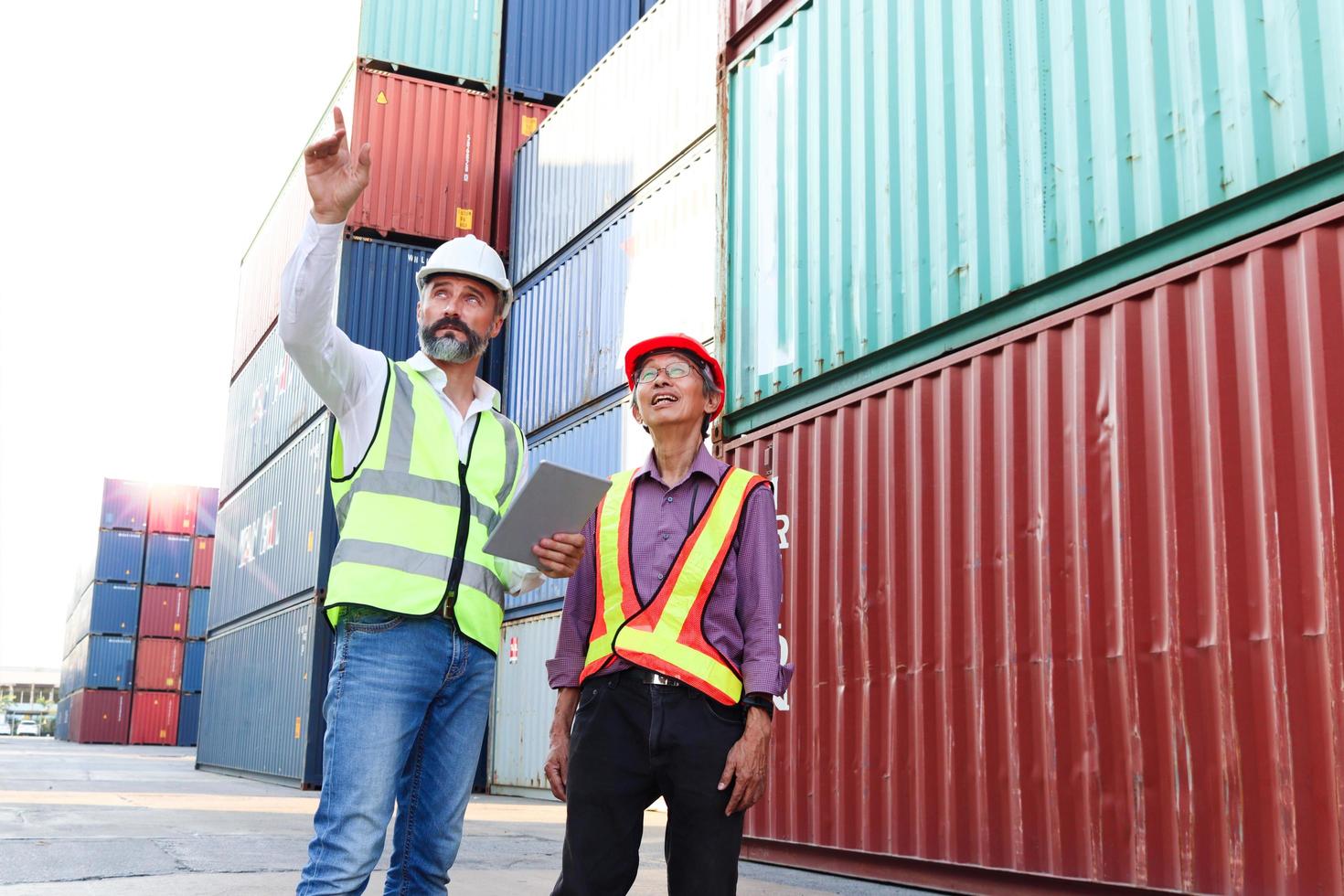 due lavoratori che indossano un giubbotto di sicurezza e un casco che discutono al cantiere di container per carichi logistici. ingegnere lavoratore asiatico anziano serio che parla con il suo capo sul posto di lavoro. foto