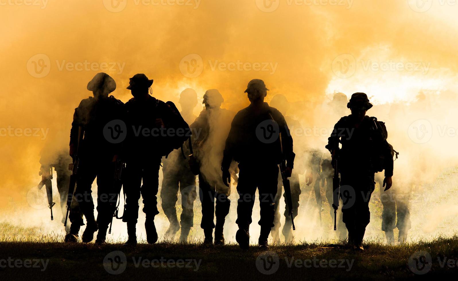 sagome di soldati dell'esercito nella nebbia contro un tramonto, squadra di marines in azione, circondato da fuoco e fumo, sparando con fucile d'assalto e mitragliatrice, attaccando il nemico foto